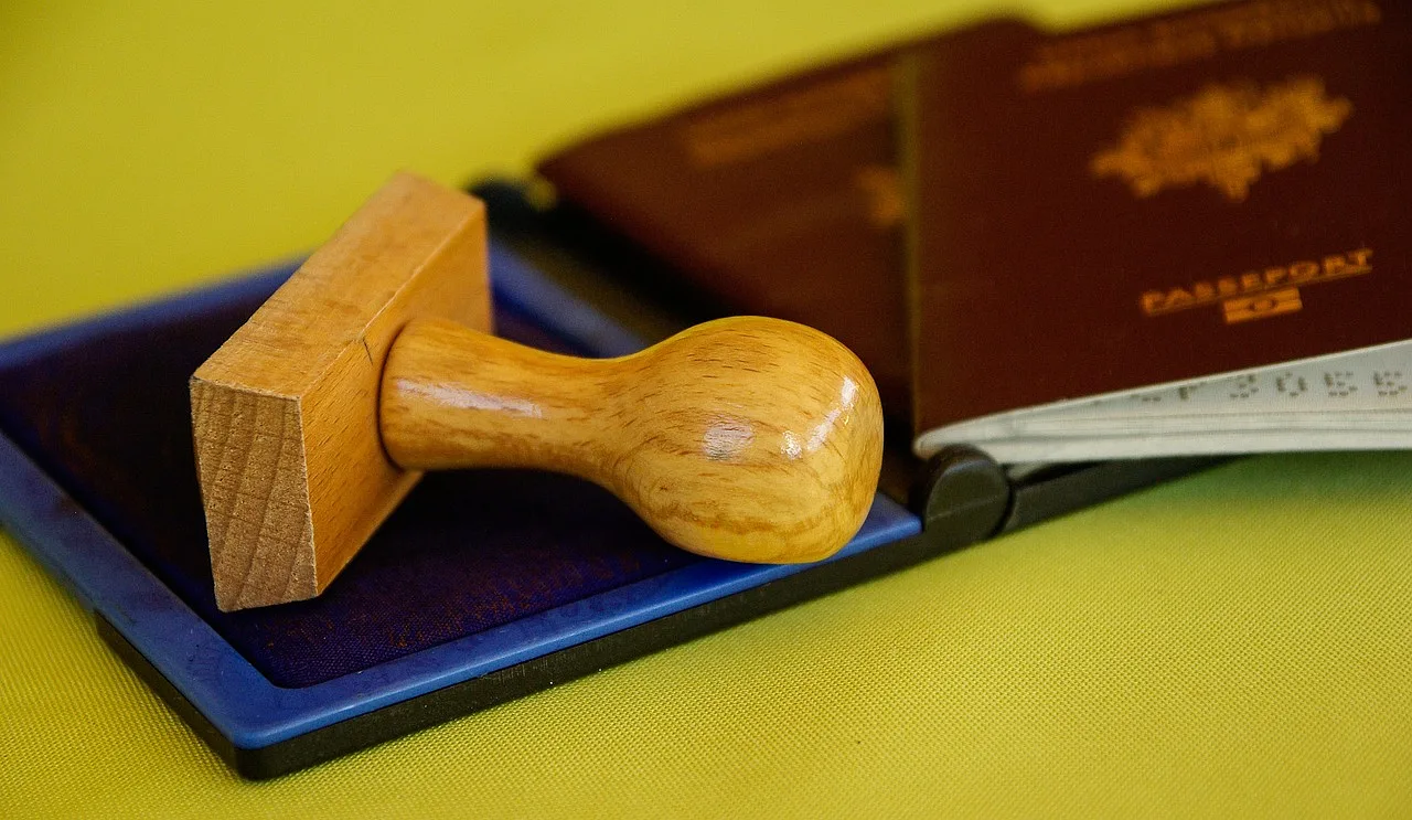 stempel na granatowej podkładce oraz dwa paszporty po prawej stronie, żółte tło