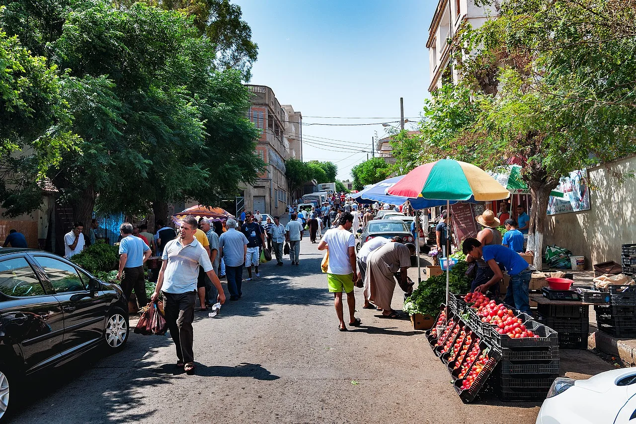 ulica pełna ludzi, po lewej czarne auto, po prawej bazar z warzywami, miasto Ain-taya, Algeria