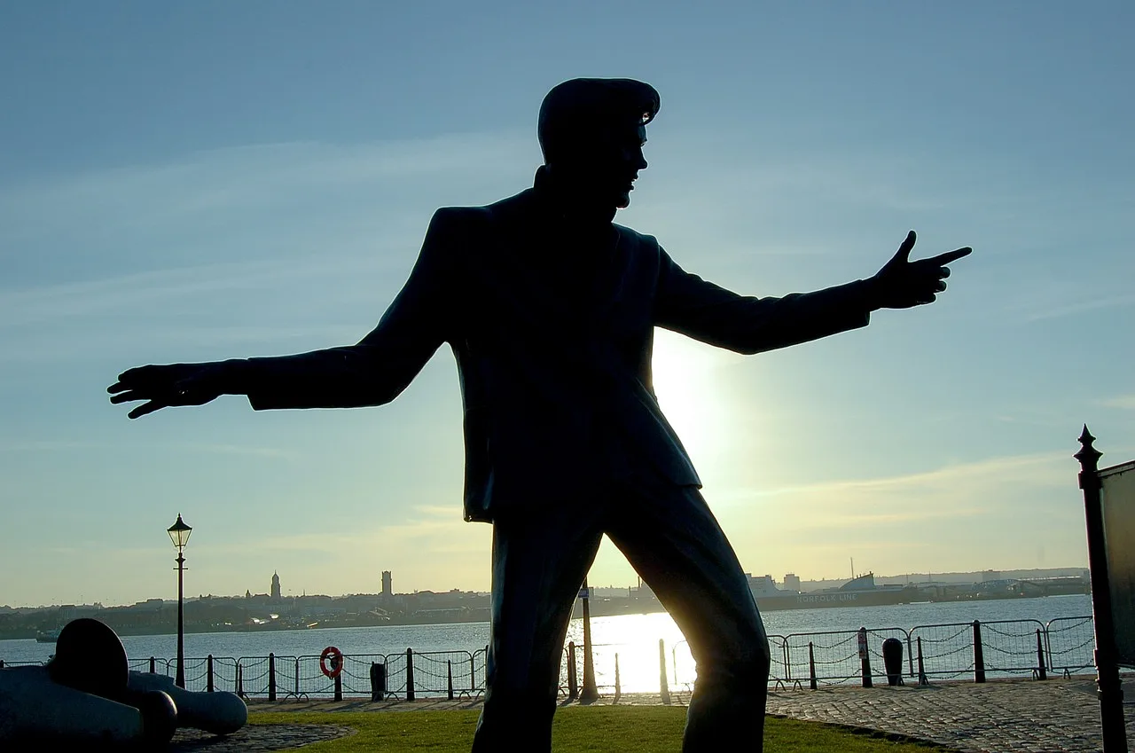 posąg Elvis'a Presley'a zasłania słońce, w tle rzeka a w oddali budynki miasta
