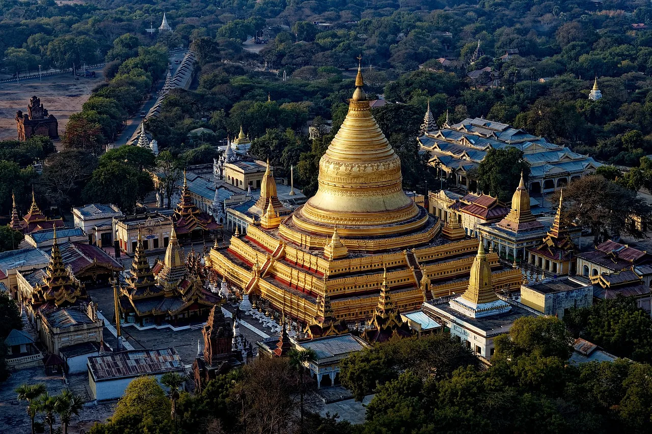 złota buddyjska stupa Shwezigon Pagoda w otoczeniu licznych zielonych drzew i pomniejszych budynków