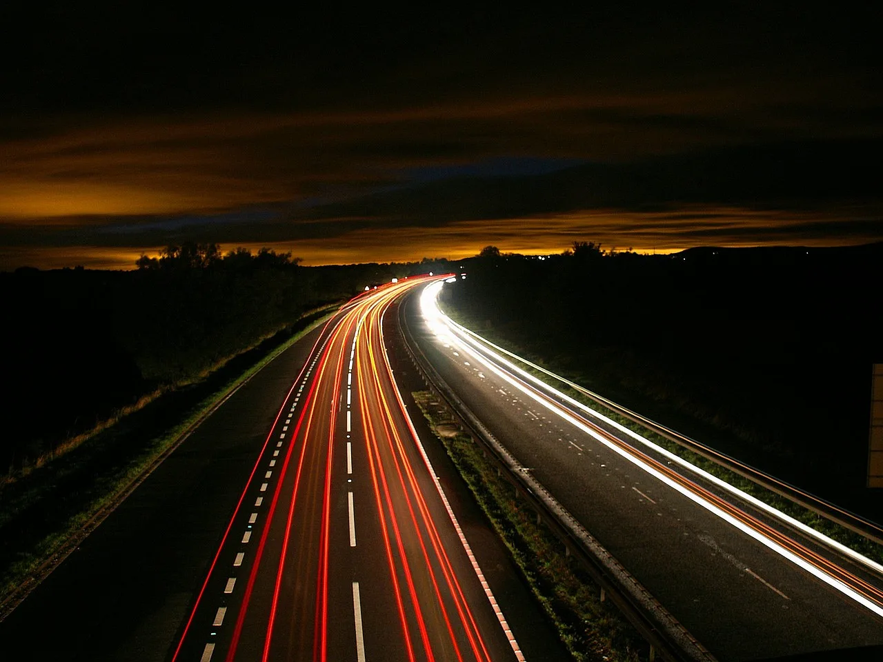 autostrada nocą, swiatla skumulowane w linie biegnace po jezdni 