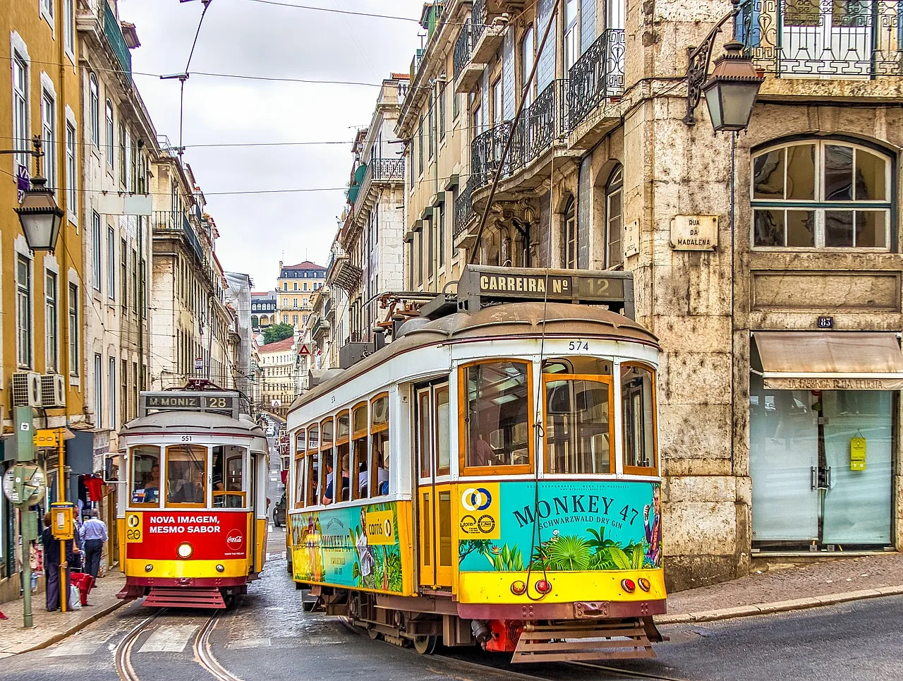 dwa kolorowe tramwaje w wąskiej uliczce różnorodnych kamienic Lizbony