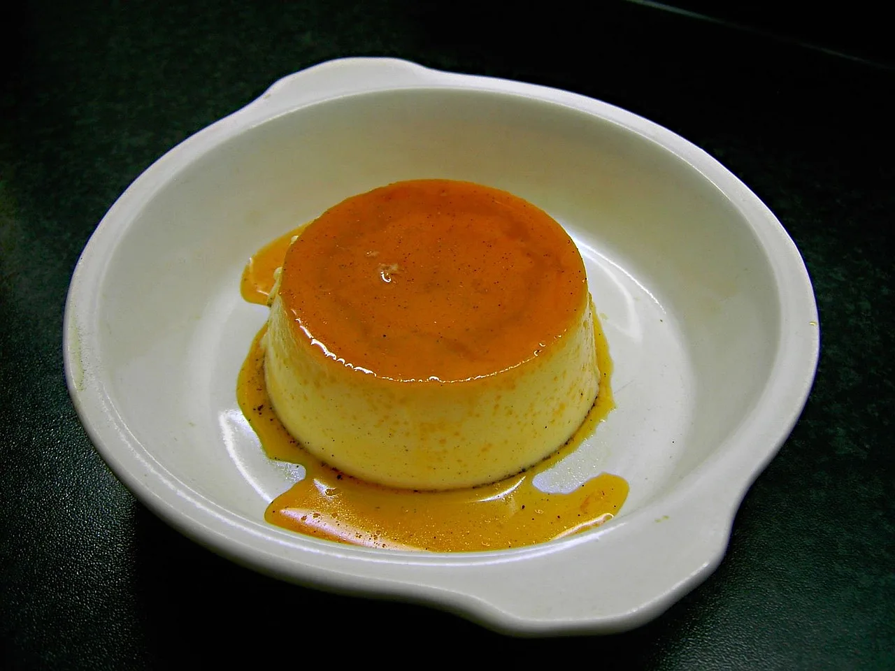 pudding waniliowy w białym naczyniu na czarnym tle