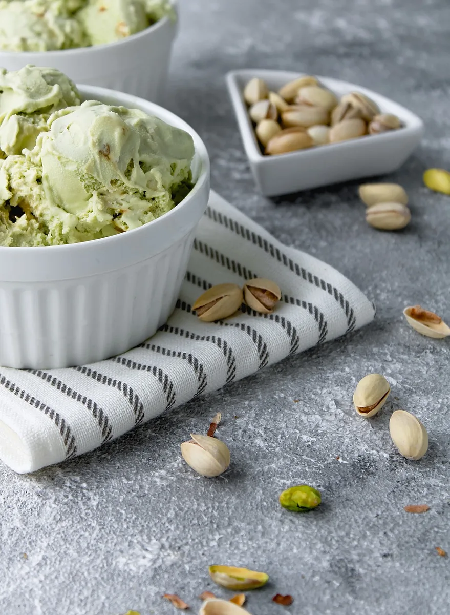 Lody pistacjowe z orzechami i świeżymi owocami na drewnianym tle, kolorowy deser idealny na lato.