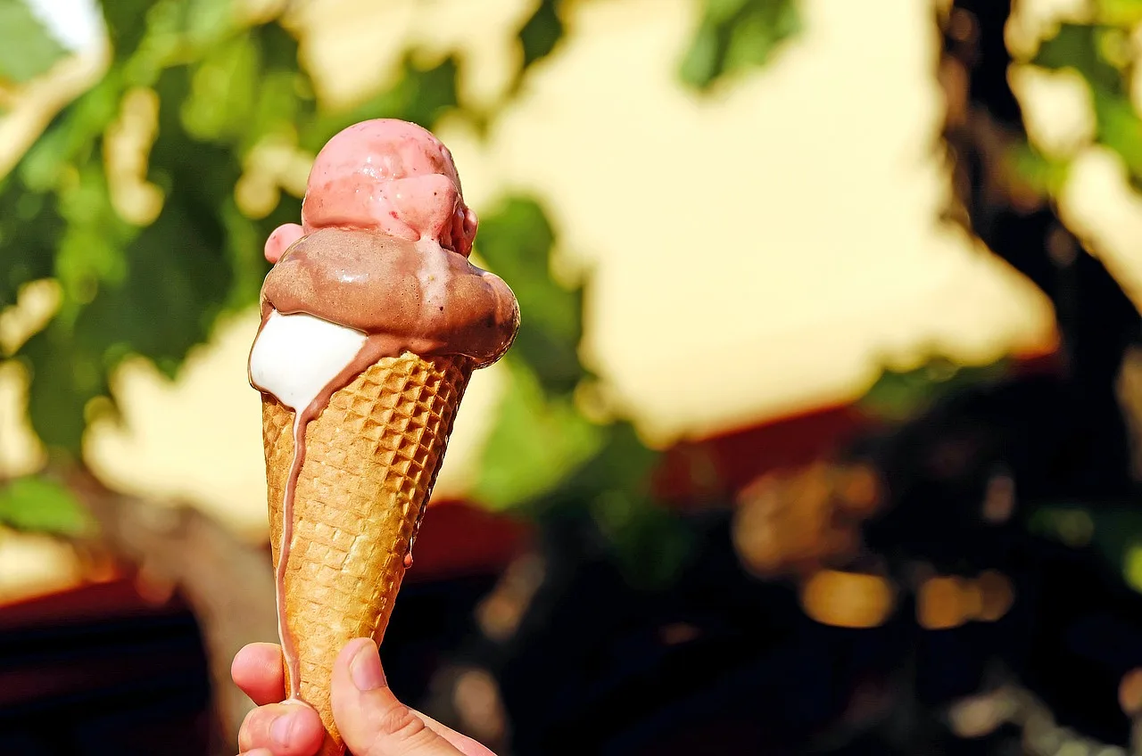 Kolorowe lody w wafelku, topniejące na drewnianym tle, przedstawiają różnorodne smaki lodów