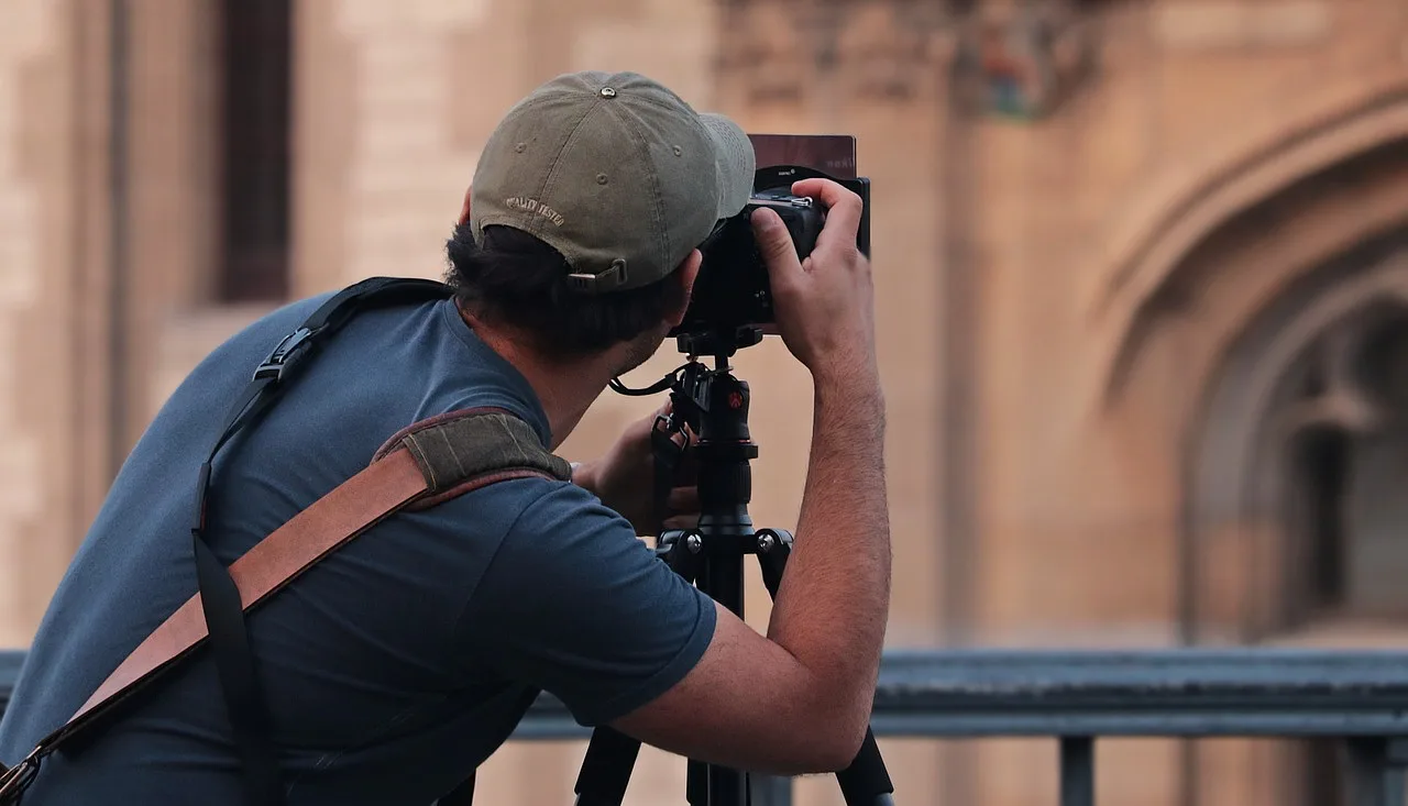 Mężczyzna trzymający aparat fotograficzny, pasjonat fotografii, uśmiechający się podczas robienia zdjęcia