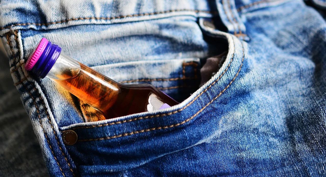 mała butelka alkoholu w kieszeni spodni dżinsowych, symbolizujący konsumpcję alkoholu
