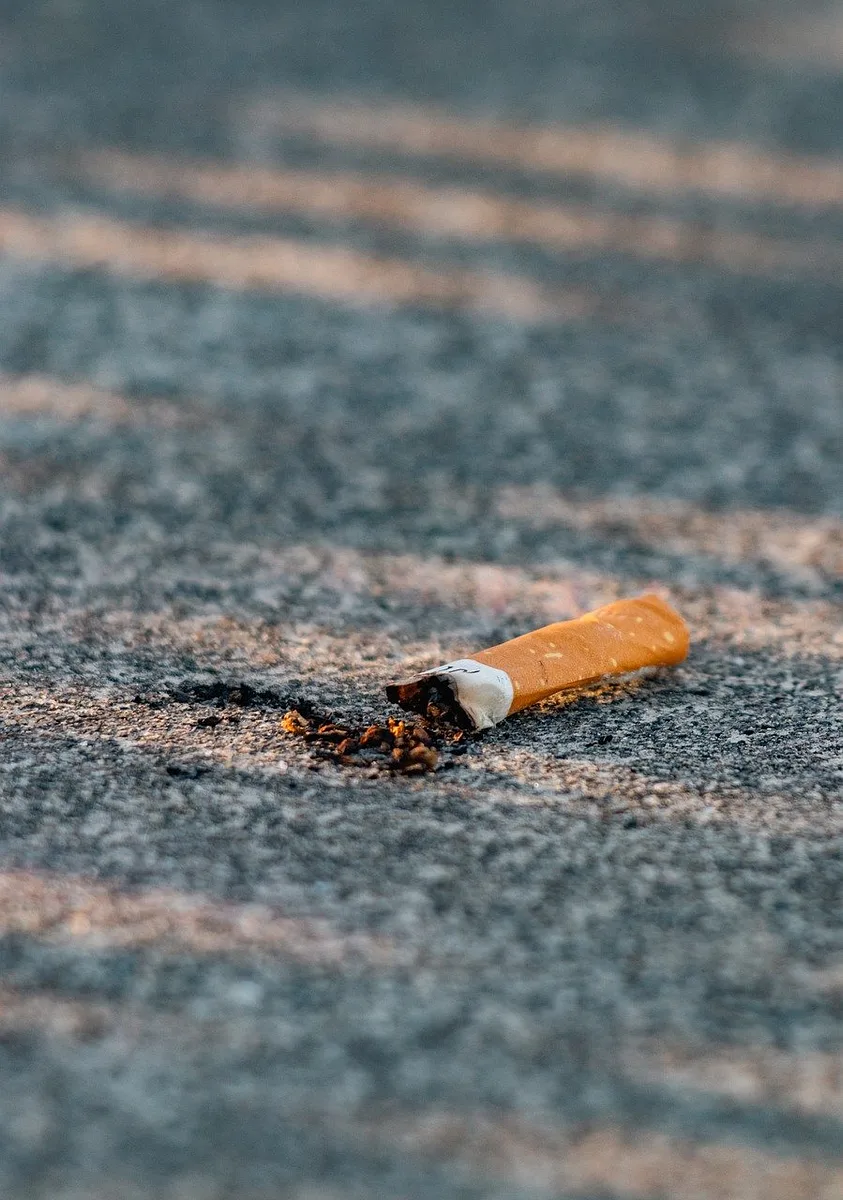 Betonowa powierzchnia z niedopałkami papierosów i odpadkami, ilustrująca problem zanieczyszczenia i palenia
