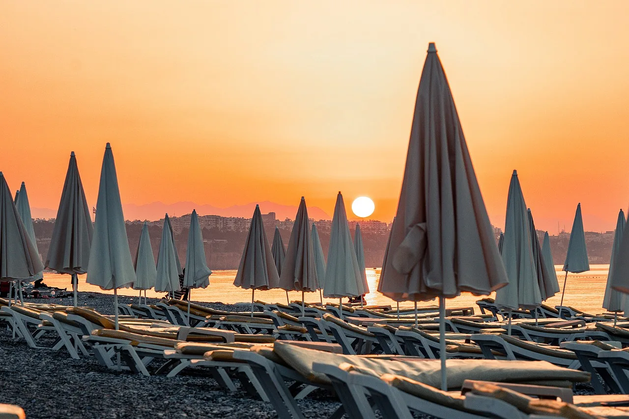 Plaża w ośrodku wypoczynkowym w Antalya, Turcja, z widokiem na morze o zachodzie słońca.