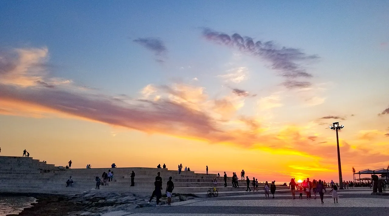 Promenada w Durrës, Albania, podczas zmierzchu, z widokiem na morze i zachód słońca, z osobami spacerującymi wzdłuż wybrzeża.