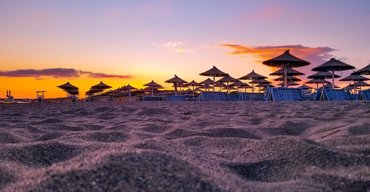 Widok na plażę w Velipoji podczas zachodu słońca z parasolem i piaskiem.