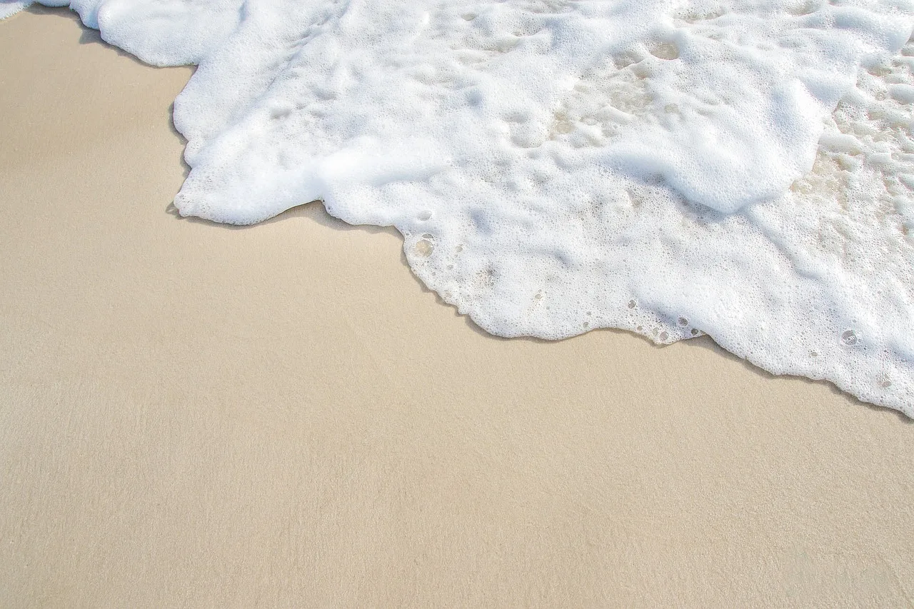 Zbliżenie na delikatną pianę morskiej fali, która spływa po piaszczystej plaży