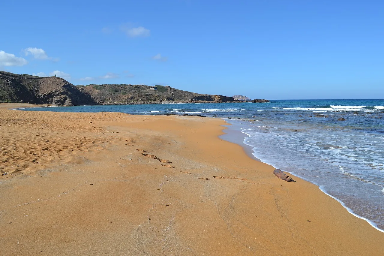 Plaża Cavalleria na Minorce z czystą wodą, piaszczystym brzegiem i malowniczym krajobrazem.